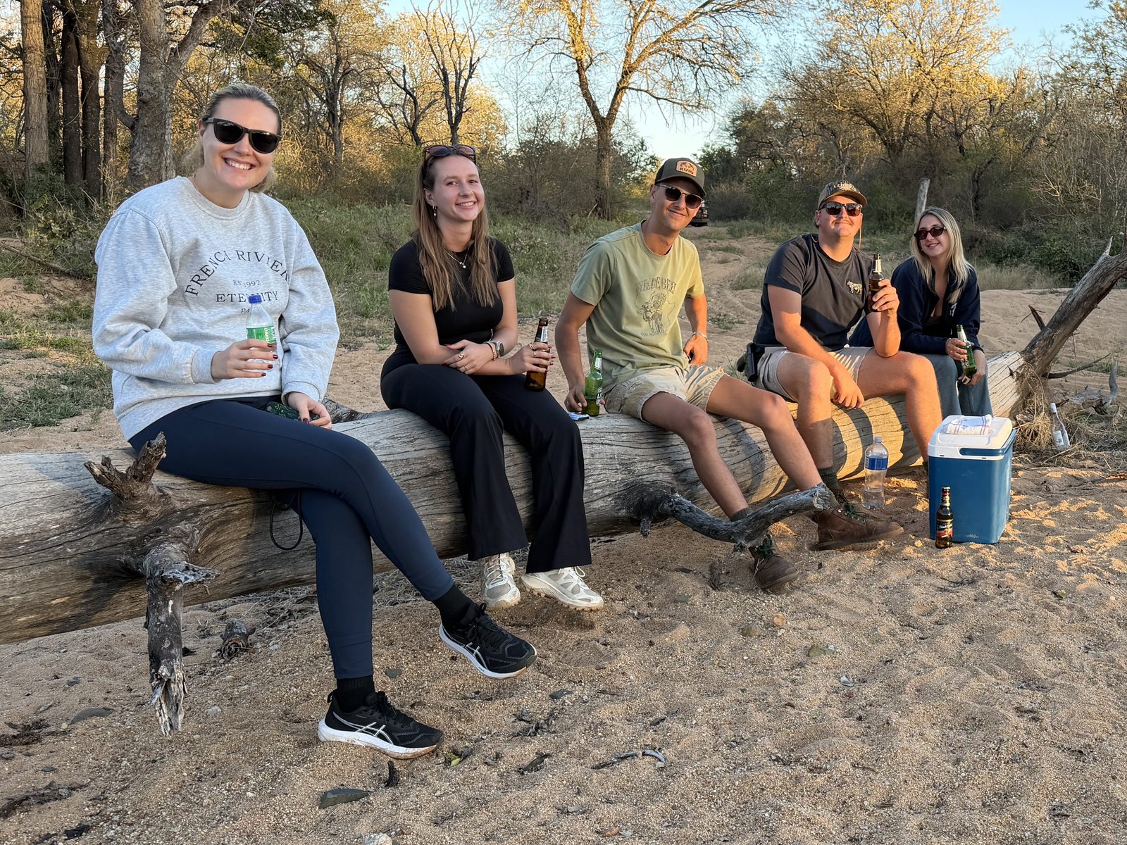 Volunteer team having sundowners on a fallen log at dusk, Greater Balepye Reserve