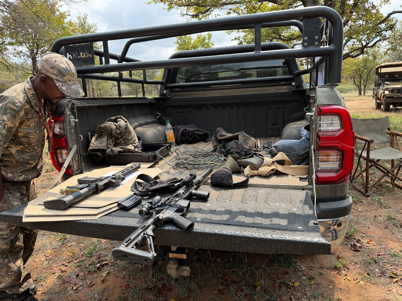 Rifles and kit laid out on the tailgate of a pickup truck, with a ranger in camouflage beside it